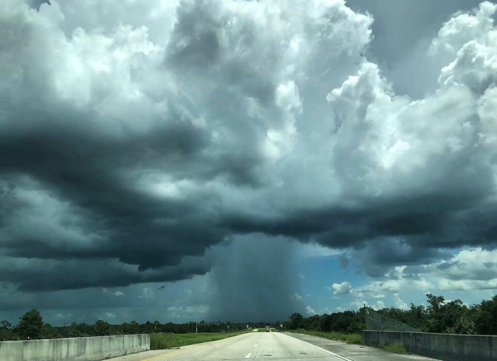 Viewed from the middle of a bridge on a road. A big gray cloud in the middle of the image with a visible gray wall of water falling from the middle.